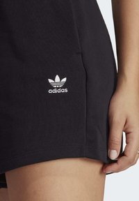 Svarta bomullsshorts med en sidficka och vitt broderat Adidas-logotyp vid fållen. Slät textur och ledig passform.