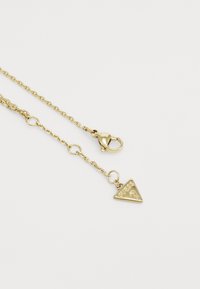 Colier din aur cu un charm triangular cu logo gravat, închidere cu cârlig de homar și lănțișoare circulare mici. Textură netedă.