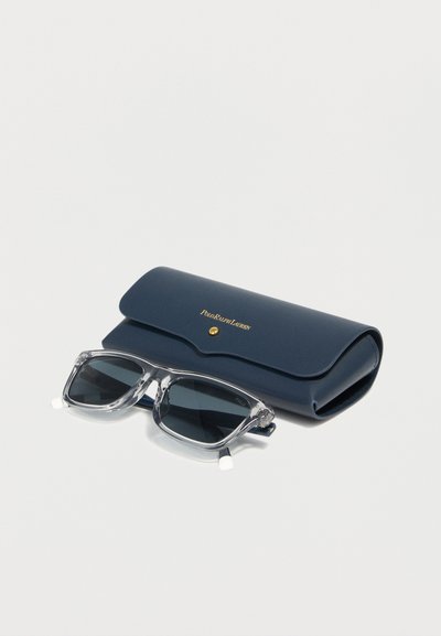 Lunettes de soleil à monture transparente avec verres foncés reposant devant un étui Polo Ralph Lauren bleu marine avec lettrage doré et fermeture à pression.