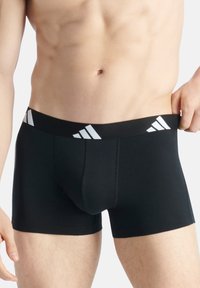 Svarta boxerkalsonger med en bred elastisk midja, prydd med tre vita diagonala ränder. Slät material med en åtsittande design.