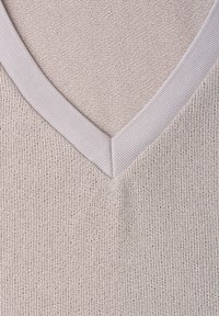 Gros plan sur un tissu beige tricoté avec bordure côtelée en V, montrant la texture et les coutures détaillées.