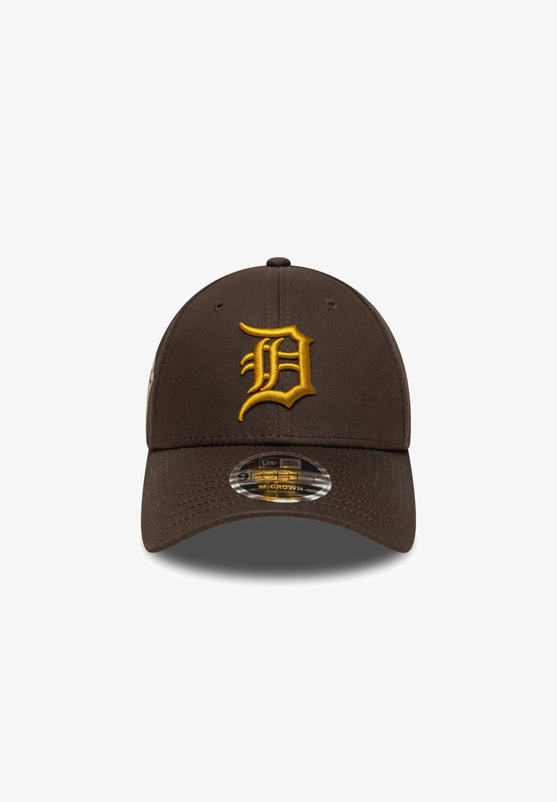 Gorra marrón con un logo bordado en amarillo con la letra "D" en la parte frontal. Cuenta con una visera curvada y ajuste en la parte posterior. El material es suave y duradero.