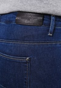 Jeans de mezclilla azul oscuro con una textura suave, que presentan costuras remalladas y una etiqueta de cintura de cuero negro grabada con "ONLY."