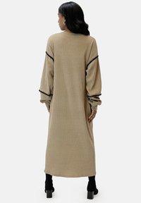 Beige ribbat långklänning med svart kant på ärmarna, som har en avslappnad passform och långa ärmar. Slät struktur, design som går ner till anklarna.