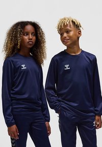 Marinblå atletiska långärmade tröjor och byxor i slätt tyg, med en logotyp på bröstet och kontrasterande sidostripes på byxorna.