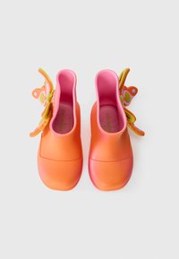 Des chaussures en caoutchouc orange et rose avec une finition lisse et brillante. Présente des accents de papillon en vert et rose sur les côtés.
