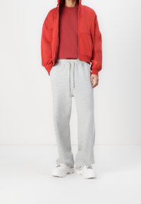 Roter Zip-Hoodie mit Kängurutasche, kombiniert mit hellgrauen Jogginghosen mit elastischem Bund und weißen Sneakers.