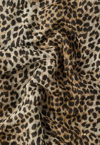Ύφασμα με λεοπάρδαλη τύπου, με μαύρες και καφέ κηλίδες σε μπεζ φόντο, που δείχνει απαλές πτυχώσεις και υφή.