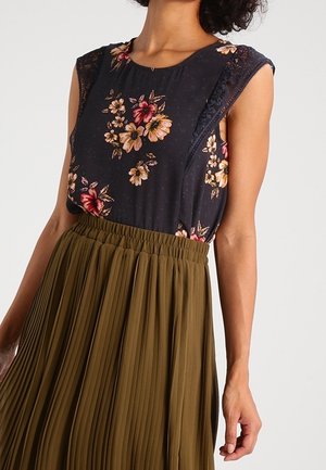 Zwart mouwloos topje met bloemenprint en kanten rand, gecombineerd met een hoge taille olijfgroene geplisseerde rok bij een staand persoon.
