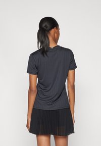 Μαύρη αθλητική μπλούζα με κοντά μανίκια και κατακόρυφες ρίγες, συνδυασμένη με πλισέ μαύρη φούστα. Λείο υλικό και ελαφρύ ύφασμα.