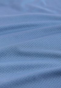 Tissu bleu clair avec de petites perforations uniformément espacées et de légères rides, mettant en valeur sa texture et son design respirant.