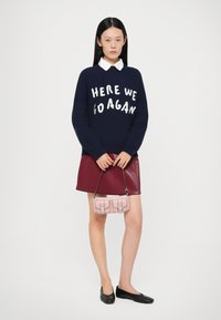Mørkeblå strikket sweater med hvid tekst, bordeaux vinyl mini nederdel, sorte flade sko og en lille lyserød crossbody taske. Balanseret styling.