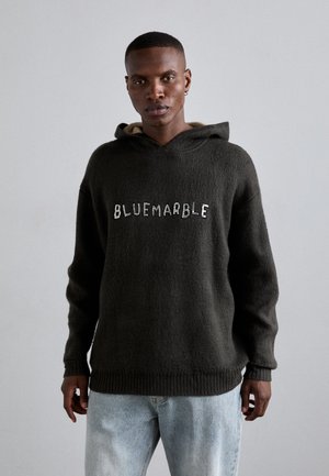 Donkergrijze, hoodie met een zachte textuur en een geribbelde zoom. De witte "BLUEMARBLE" opdruk staat gecentreerd op de voorkant. Lichtblauwe jeans.