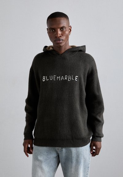Sudadera con capucha de color gris oscuro, con una textura suave y dobladillo acanalado. La inscripción "BLUEMARBLE" en blanco está centrada en la parte delantera. Jeans de color azul claro.