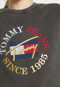 Tmavě šedá mikina s žebrovaným výstřihem. Obsahuje odvážné, multikolorové grafiky: "TOMMY JEANS", logo s červenými, bílými, modrými a zlatými akcenty.