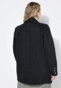 Mustaharajali denim-jakki, jolla on suoraviivainen leikkaus, suuret kaulukset ja napitettavat hihansuut. Rakenne-elämys ja saumaton selkäosa, rento istuvuus.