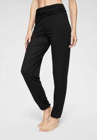 Zwarte, loszittende broek met een brede, omslagbare tailleband. Soepele, rekbare stof. Enkel-lengte met een taps toelopend ontwerp en zonder zichtbare patronen.