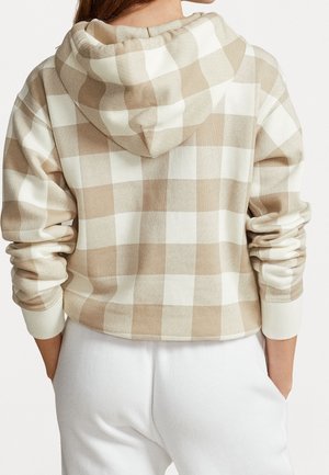 Persoon die een beige-wit geruit capuchontrui met lange mouwen en een witte broek draagt, gezien vanaf de achterkant.