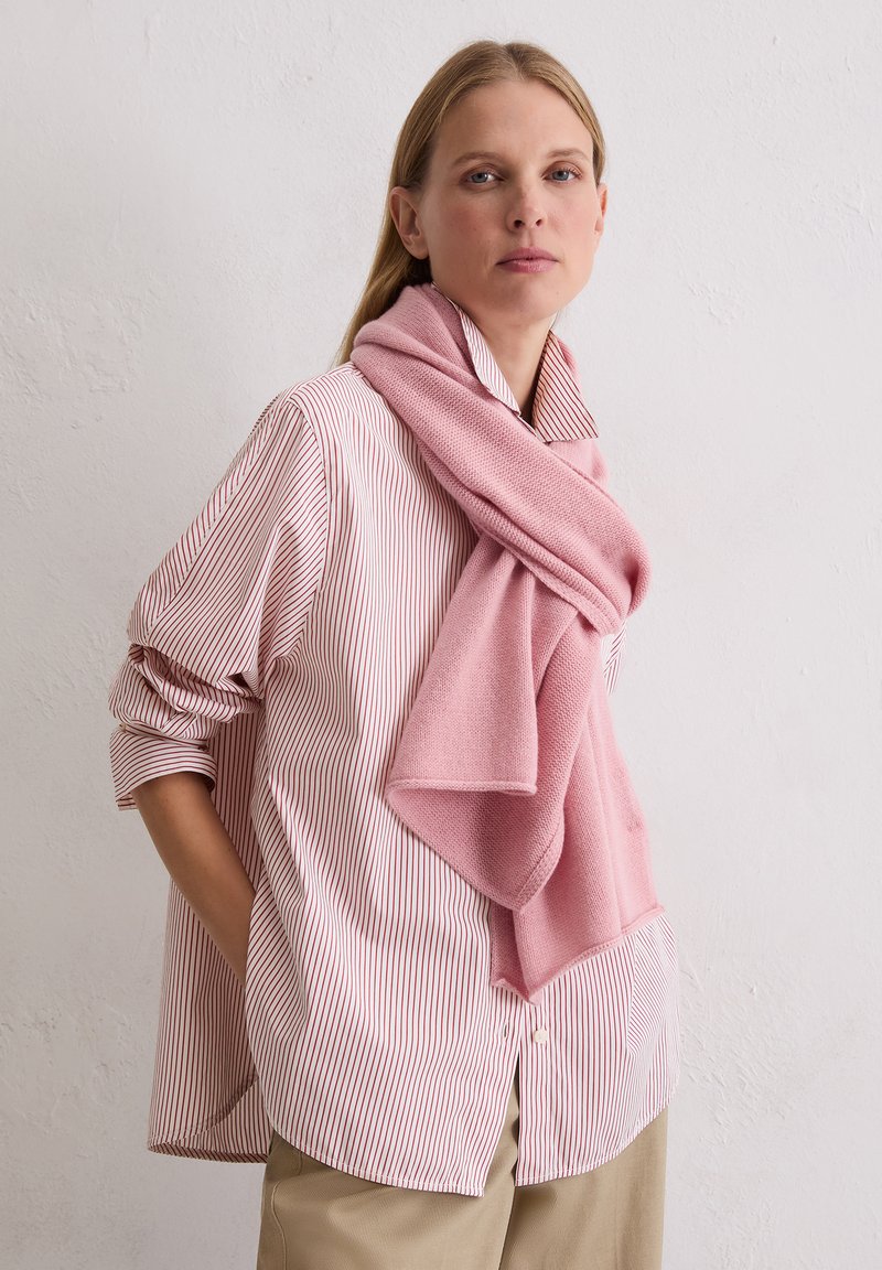 Écharpe rose clair en matière douce, portée sur une chemise rayée avec des lignes rouges. L'écharpe se drape élégamment autour du cou.