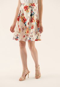 Blommig A-linje-formad kjol i krämfärg med klara röda, blå och gula blommor. Tyget är lätt, med en figursydd midja och veckad design.