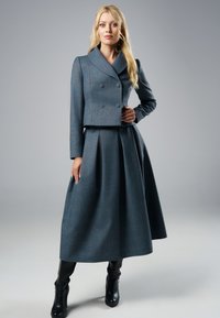 Szary kraciasty żakiet o kroju krótkim z podwójnymi guzikami, zestawiony z pasującą plisowaną spódnicą midi. Noszony z dopasowanymi czarnymi botkami na obcasie.