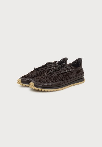 Paire de baskets tressées marron foncé avec semelles en caoutchouc beige et lacets élastiques réglables sur fond blanc.