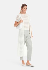 Weißer, gestrickter Cardigan über einem Kurzarm-Shirt, kombiniert mit hellgrauen gestreiften Hosen und weißen Ballerinas. Einfaches Design, leichtes Material.