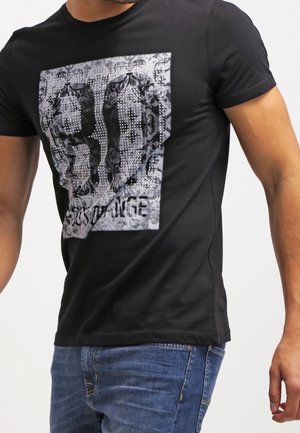T-shirt nera a maniche corte con un grande motivo grafico in scala di grigi e la scritta "EXCHANGE", indossata da una persona con jeans blu.