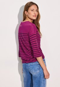 Magenta ja tumma purppuranraidallinen paita, jossa on 3/4-hihat, pyöreä kaula-aukko ja rento istuvuus, yhdistettynä vaaleansinisiin farkkuihin.