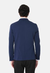 Blazer blu navy con una texture liscia, design slim fit, fessura singola sul retro e due tasche frontali. Maniche lunghe con dettagli a bottoni.