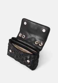 Bolso de mano negro tejido con un exterior texturizado, que cuenta con un único compartimento forrado en tela beige y cierres de botón en tono dorado.