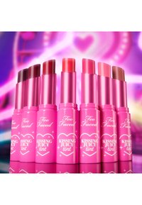 Eight lip tints in vibrant pink packaging with a heart design. Each has a twist-up applicator with varying shades from dark to nude.