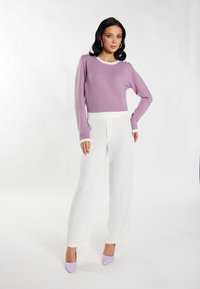 Lila langemouwen trui met witte afwerking, gecombineerd met witte wijde broek en paarse puntige hoge hakken.
