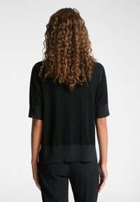 Top noir à manches courtes avec une texture lisse, présentant un ourlet arrondi et des accents côtelés contrastants sur les manches et le bas.