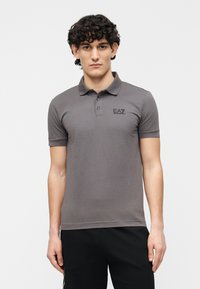 Grå poloshirt med korte ærmer, to-knaps placket og sort logo på brystet; glat tekstur, tætsiddende design og åndbart stof.