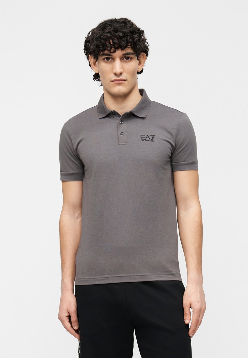 Grå poloshirt med korte ærmer, to-knaps placket og sort logo på brystet; glat tekstur, tætsiddende design og åndbart stof.