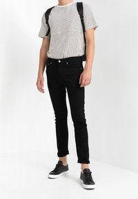 Randig kortärmad skjorta med ljus botten och mörka ränder, i kombination med svarta slim fit-jeans och svarta sneakers; minimalistisk ryggsäck.