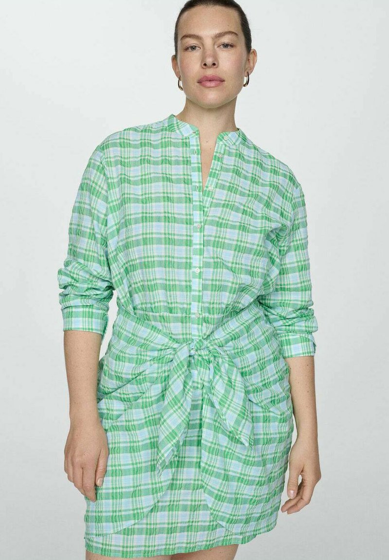 Abito camicia a quadri verde e blu con cintura da annodare, maniche lunghe e chiusura frontale con bottoni. Tessuto leggero con una consistenza morbida.