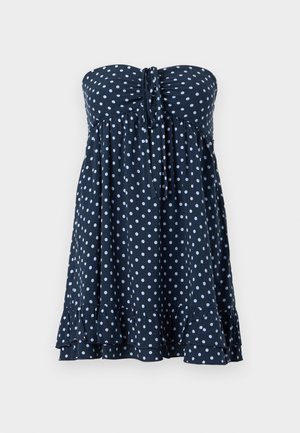 Marineblauwe strapless jurk met witte polka dots, een strik in het midden en een gerimpelde zoom.