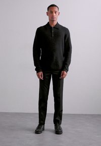 Schwarzer Strick-Polo-Pullover mit Kragen und drei Knöpfen, kombiniert mit maßgeschneiderten schwarzen Hosen und schwarzen Sneakern. Glatte Textur.