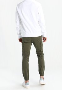 Felpa bianca a maniche lunghe con maniche raglan, abbinata a pantaloni cargo verde oliva con tasche laterali e polsini elasticizzati, indossata con sneakers bianche.