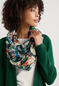 Il foulard infinito floreale presenta colori vivaci tra cui verde, arancione e blu su uno sfondo chiaro, realizzato in un tessuto morbido e strutturato.