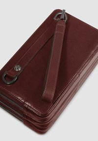 Cartera de cuero burdeos con una textura suave, que cuenta con tres compartimentos con cremallera, una correa desmontable y un acento de hardware en tono plateado.