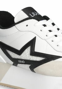 Sneaker bianca con pelle testurizzata, dettagli neri e un design a stella glitterato. Presenta un colletto imbottito e un logo audace sulla linguetta.