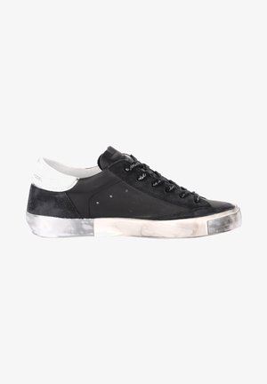 Baskets noires en matériaux daim et cuir, avec une semelle intermédiaire texturée, un design à lacets et une touche de blanc au niveau du talon.