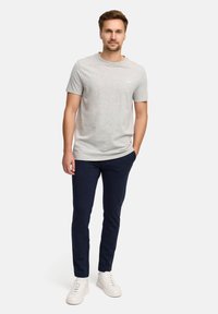 Grijze katoenen t-shirt met een ronde hals, marineblauwe slim-fit broek en witte sneakers. Subtiel logo op de borst.