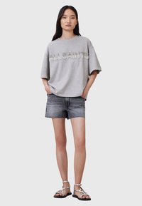 Grå oversized T-shirt med "ALLSAINTS" i rhinsten, parret med sorte denimshorts og sølvfarvede spændte sandaler.