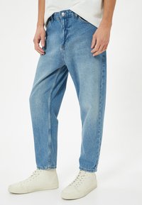 Světlé modré džínové kalhoty s volným střihem, obsahující zapínání na knoflík a zip, přední kapsy a rovný střih nohavic.