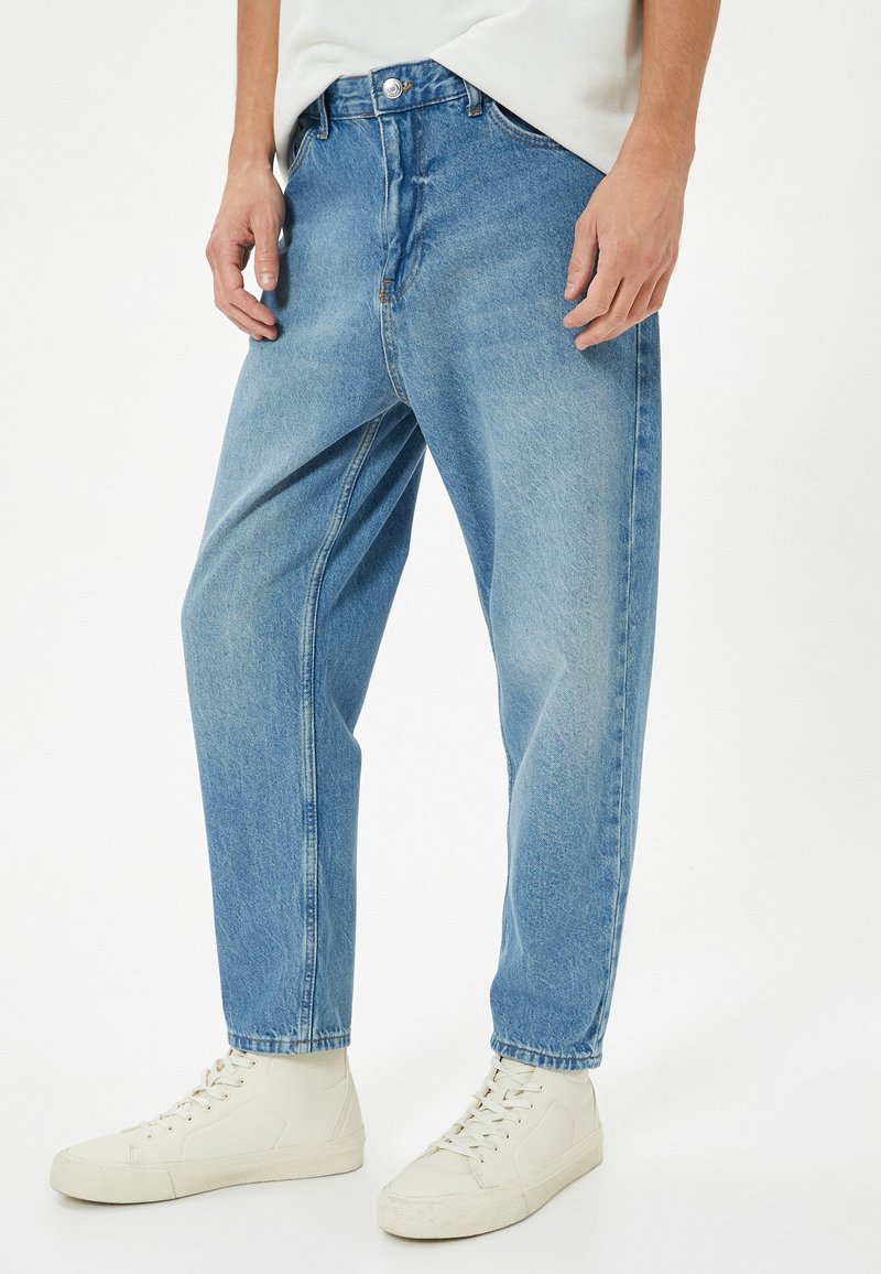 Světlé modré džínové kalhoty s volným střihem, obsahující zapínání na knoflík a zip, přední kapsy a rovný střih nohavic.