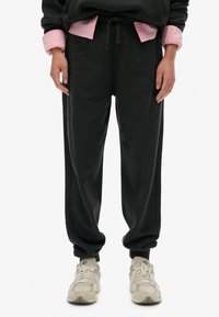 Sorte sweatpants med snøre i taljen, tapered cuffs og sidesømmer, parret med lyse sneakers. Tekstureret stof, afslappet pasform.